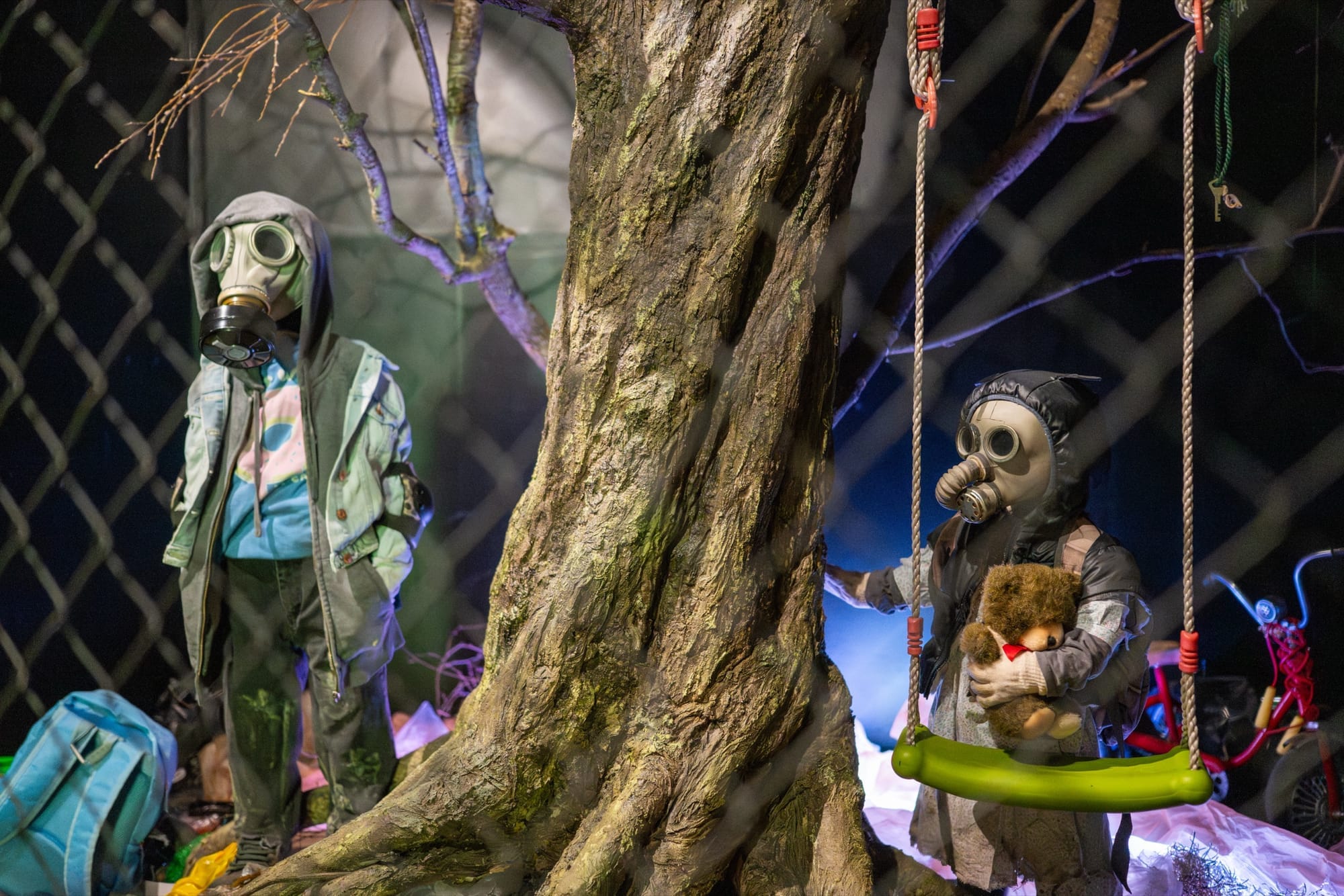 Figures in gas masks beneath a bare indoor tree
