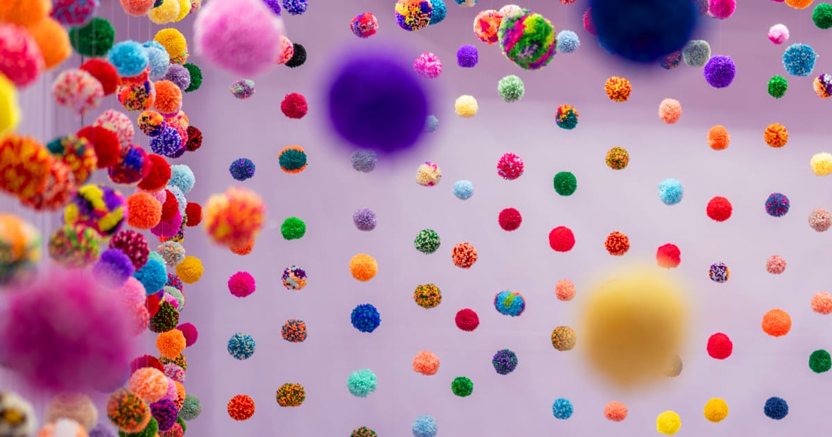 Rows of colourful pom-poms suspended against a soft pink wall